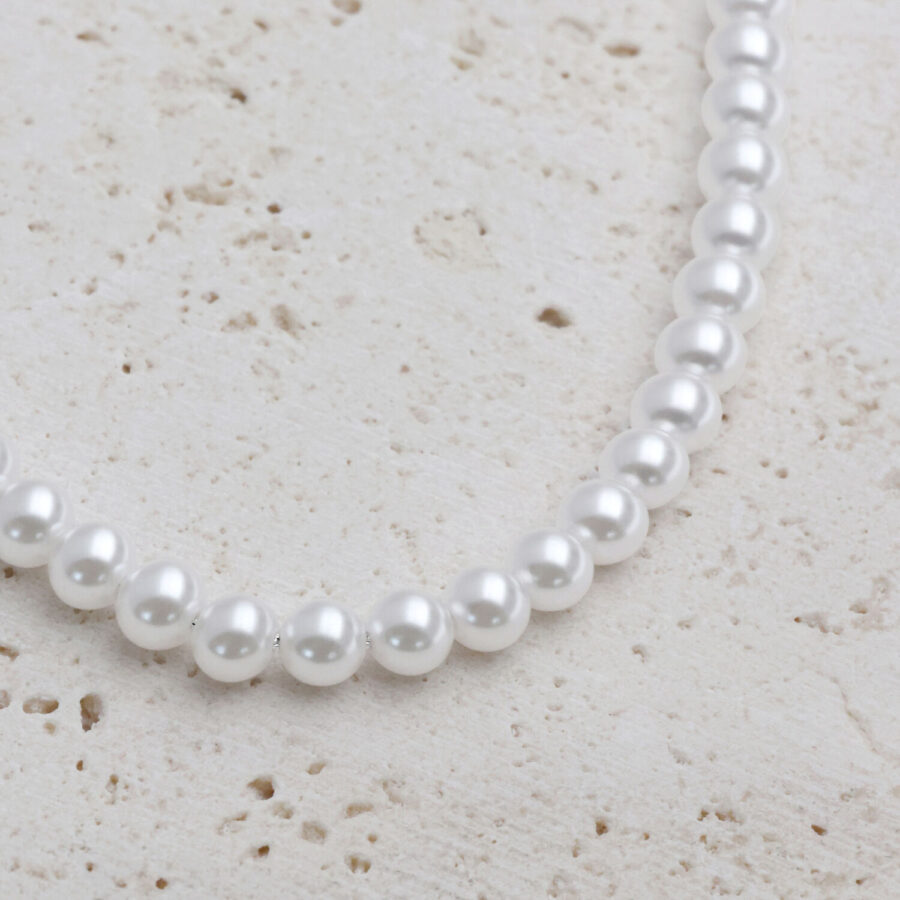 Collar de perlas sintéticas plateadas sobre fondo de piedra clara