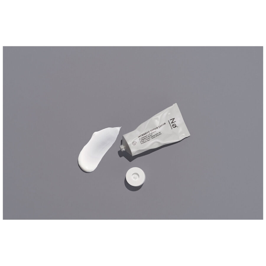 Tubo gris-blanco de la Crema Reparadora Intensiva de Nø Cosmetics con tapa quitada sobre fondo gris