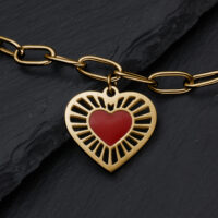 Pulsera Sacred Heart dorada con corazón rojo Pulsera de metal dorado con colgante en forma de corazón y corazón rojo sobre fondo de pizarra