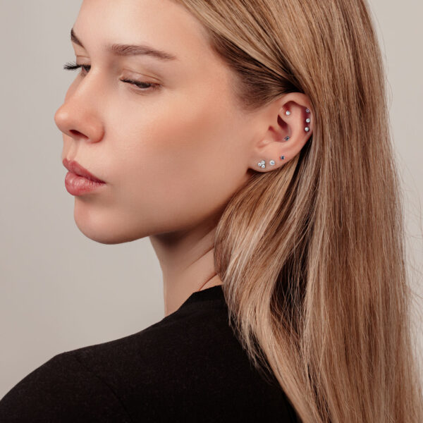 Mujer con varios piercings y pendiente de bola de cristal sobre fondo claro