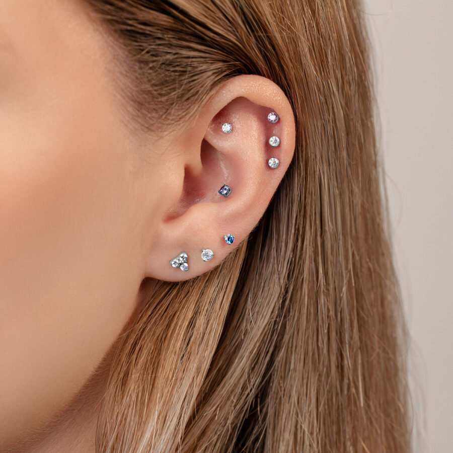 Primer plano de una oreja con varios piercings, incluyendo un accesorio 3-Prong en colores cristal