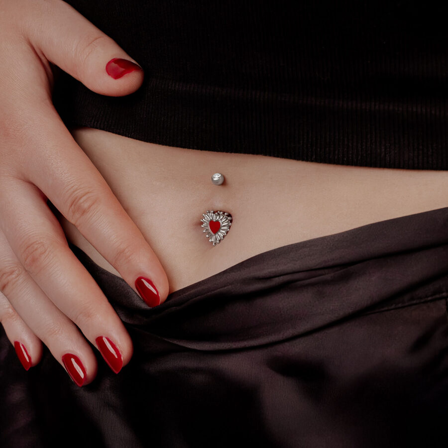 Mujer con esmalte de uñas rojo mostrando Sacred Heart Bananabell en el ombligo
