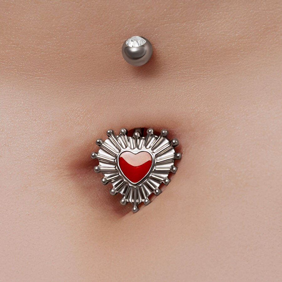 Piercing de ombligo con diseño de corazón rojo y acentos plateados sobre piel