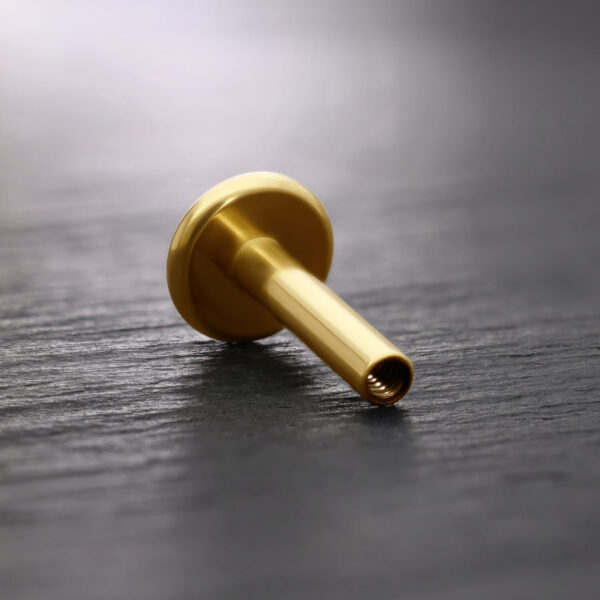 Labret de titanio dorado sobre fondo oscuro, inclinado