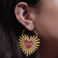 Goldene Barbed Wire Sacred Heart Creolen am Ohr einer Frau vor neutralem Hintergrund