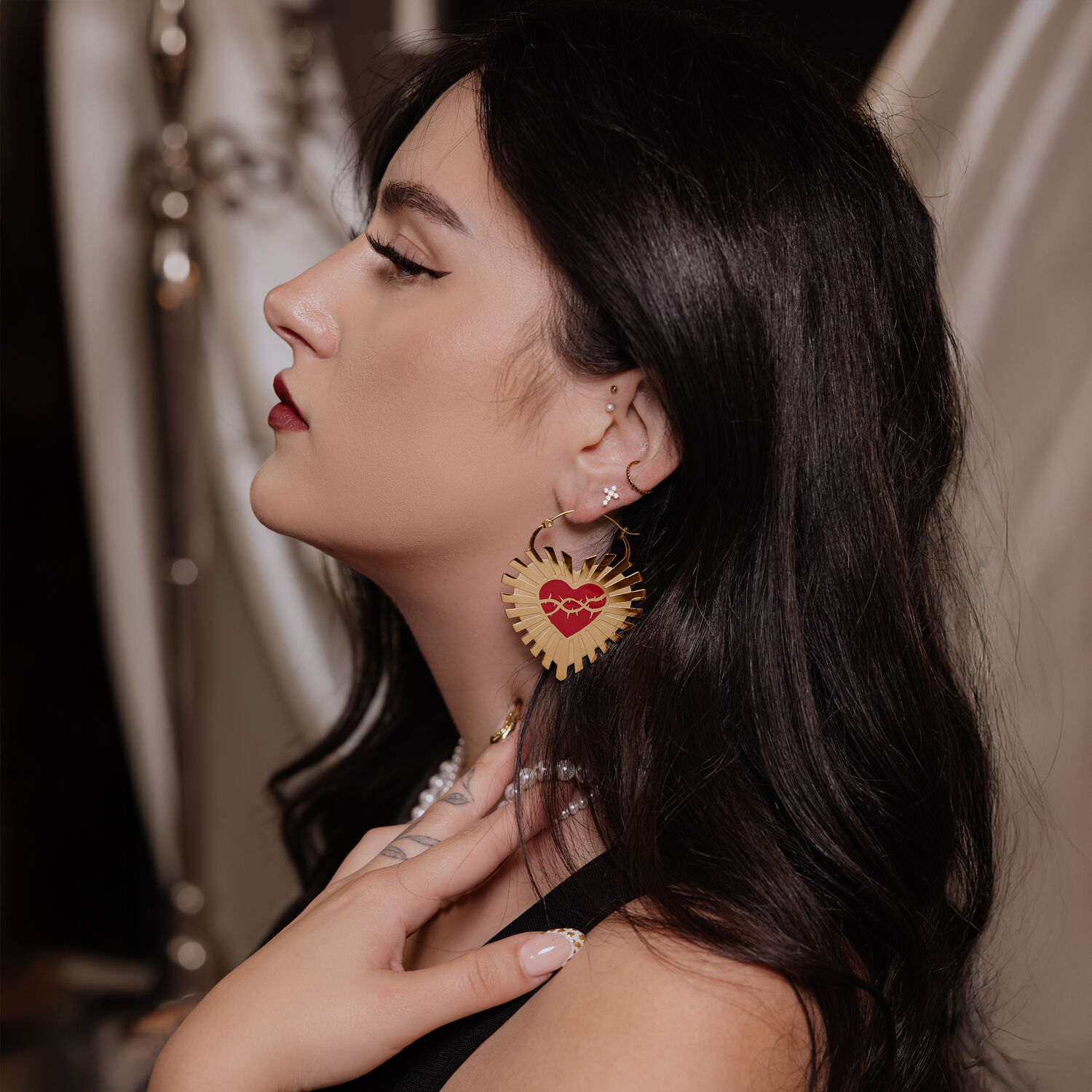 Goldene Herz-Ohrringe mit Stacheldraht in Ohr einer Frau mit dunklem Haar