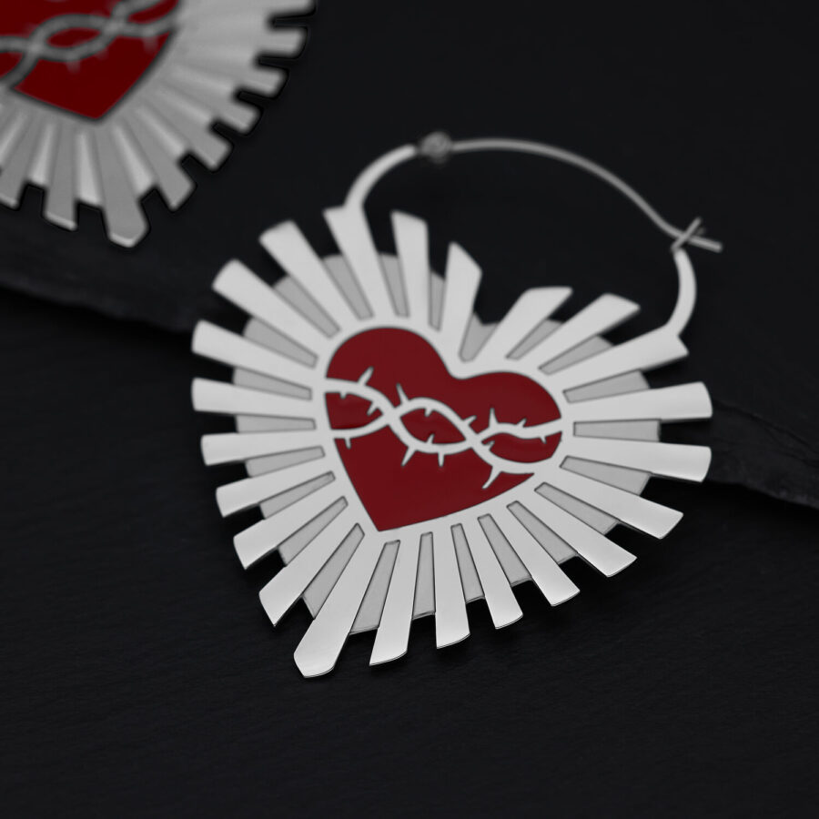 Aros plateados en forma de corazón con corona de espinas roja sobre fondo negro