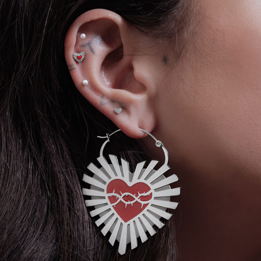 Pendientes plateados en forma de corazón con diseño de alambre de púas en una oreja