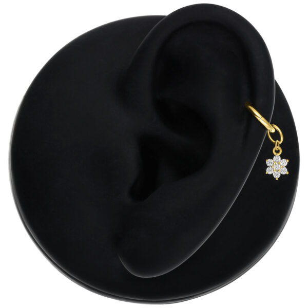 Colgante de flor dorado con moissanita en una oreja sobre fondo negro
