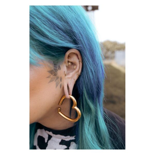 Piercing Bananabell dorado en oreja con cabello azul y pendiente de corazón.