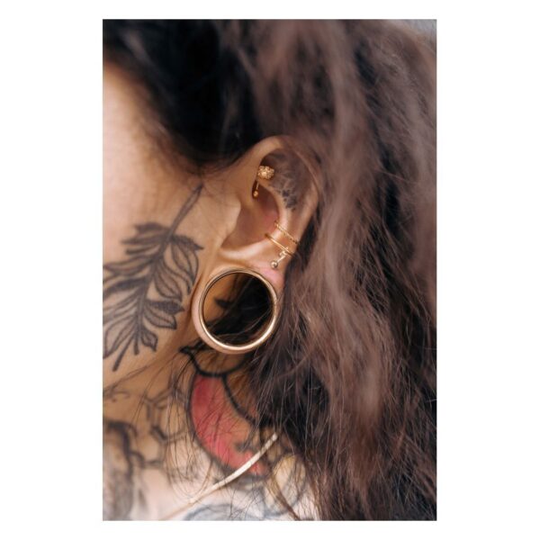 Piercing Bananabell en Oro Rosa en la oreja con tatuaje de fondo