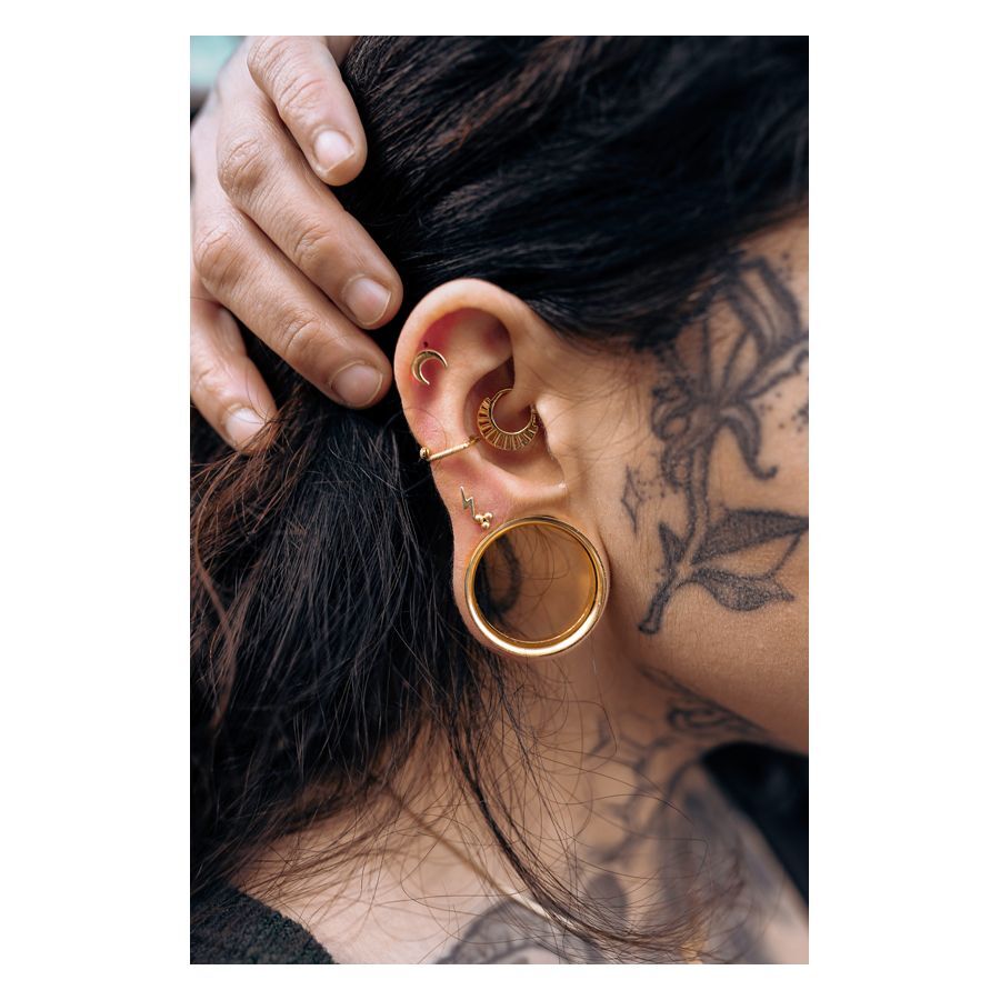 Goldener Tunnel mit Innengewinde im Ohr einer Person, umgeben von weiteren Piercings und Tattoos