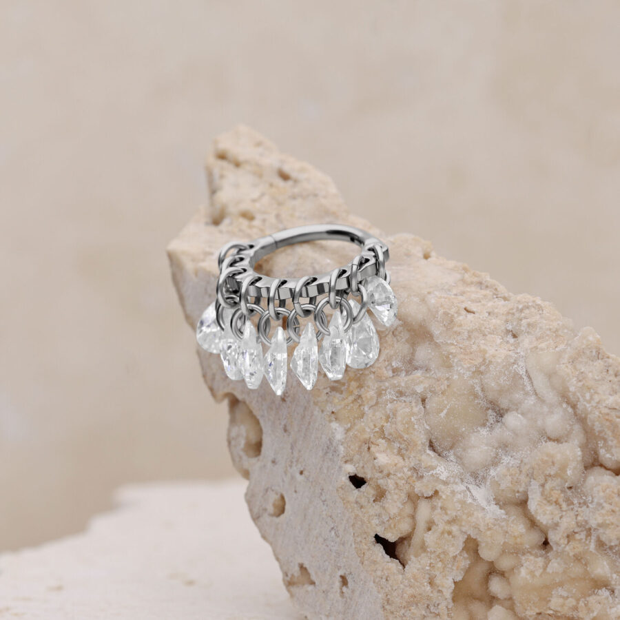 Anillo de piercing plateado con cristales claros sobre fondo beige