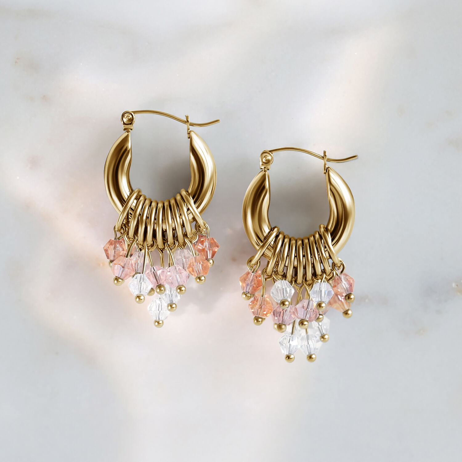 Pendientes Glamour Hoops de oro con cristales rosas y transparentes sobre fondo de mármol