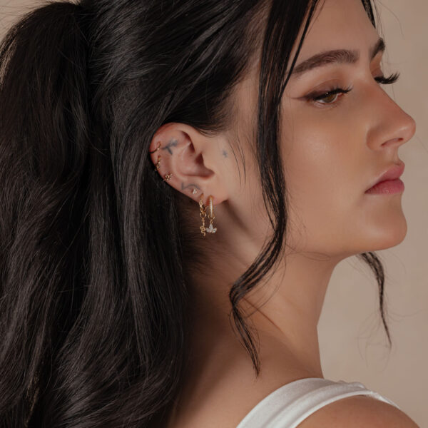Mujer con anillo de bisagra de oro de 18K en la oreja, perfil lateral, cabello oscuro