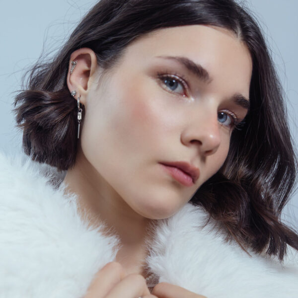 Mujer con accesorio de piercing Push Fit elegante en plata en el cartílago de la oreja, fondo blanco