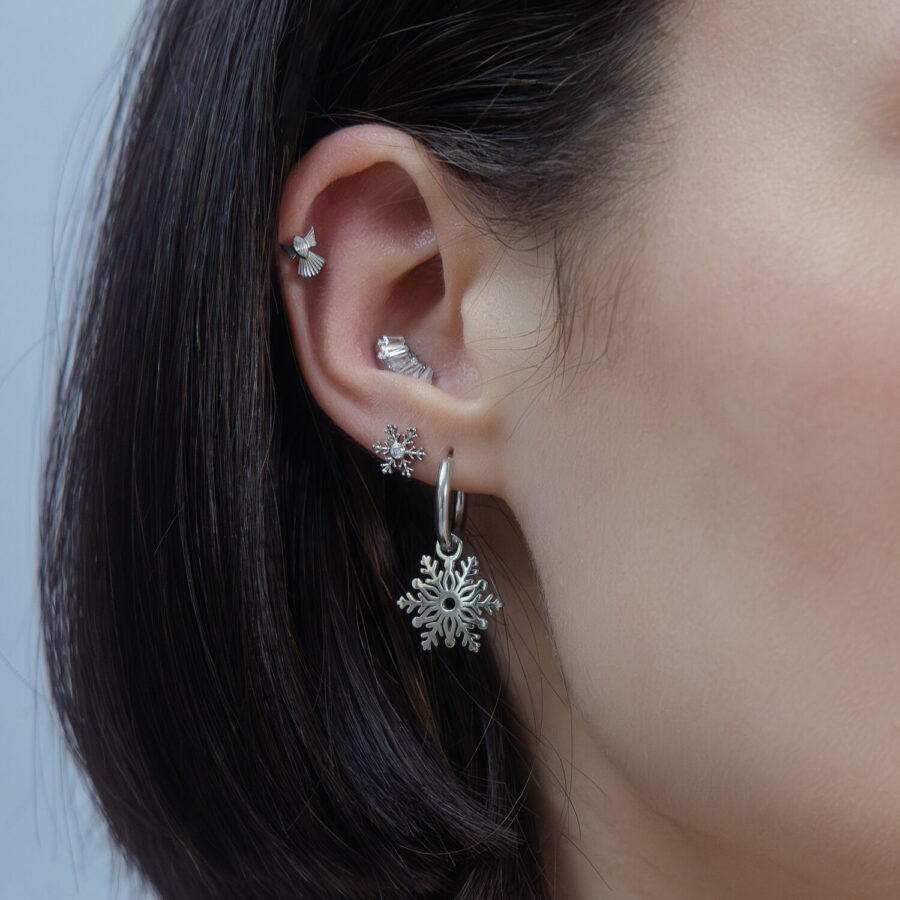 Oreja con varios piercings plateados, diseño de copo de nieve, sobre fondo neutro