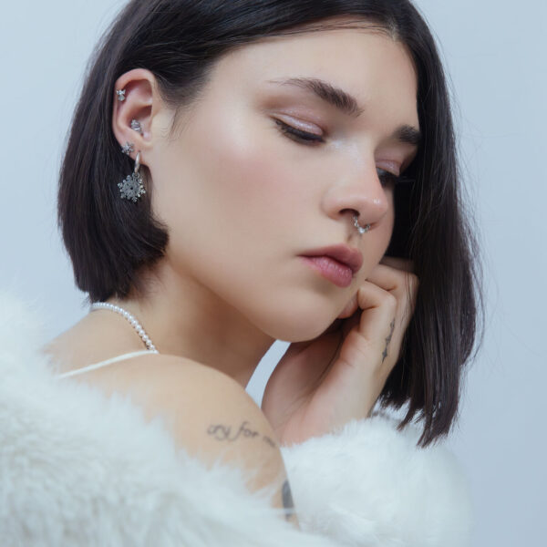 Mujer con piercing de copo de nieve plateado en la oreja frente a un fondo claro
