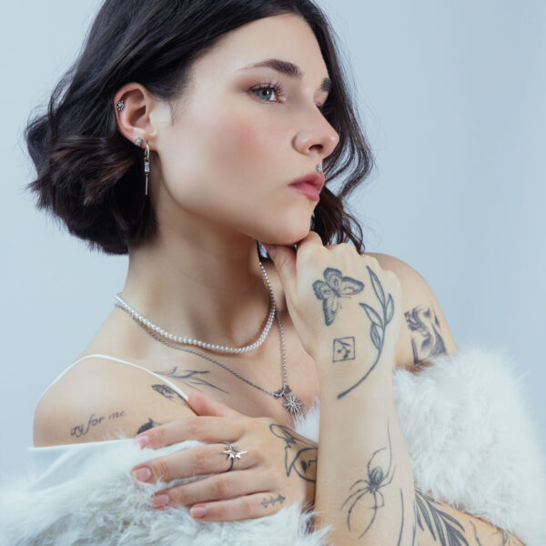 Mujer con varios piercings, incluyendo un Sunburst plateado en la oreja, sobre fondo neutro