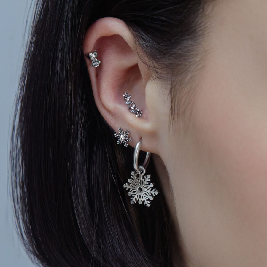 Primer plano de una oreja con varios piercings plateados en diferentes diseños y cristales