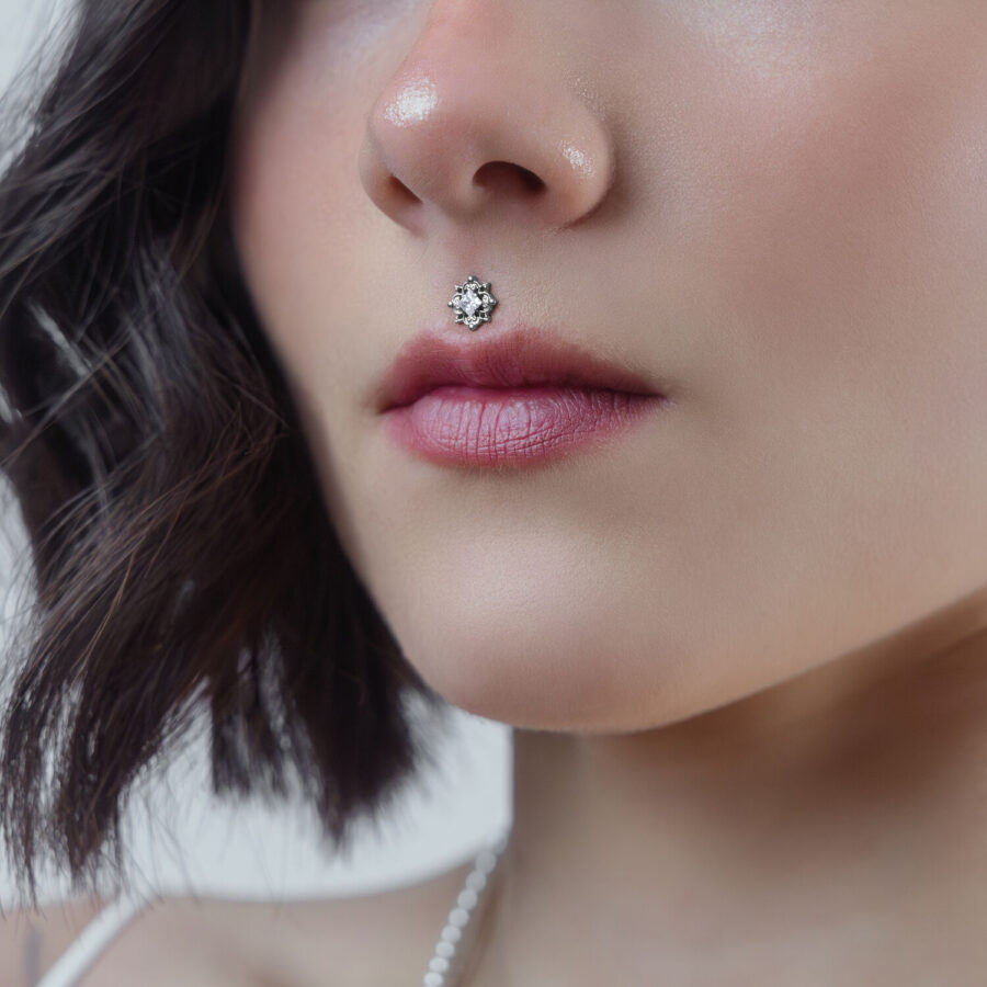 Primer plano de un accesorio de piercing de cristal plateado en el piercing Medusa de una mujer sobre un fondo neutro