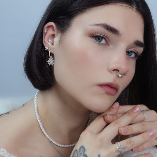 Mujer con varios piercings, incluyendo un aro Snow Angel plateado en la oreja, sobre un fondo neutro.