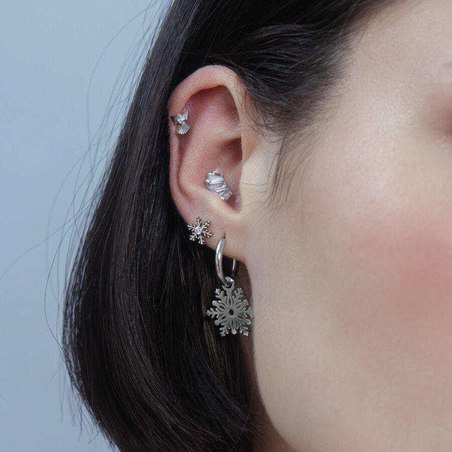 Mujer con piercing de Snow Angel plateado en la oreja, fondo neutro