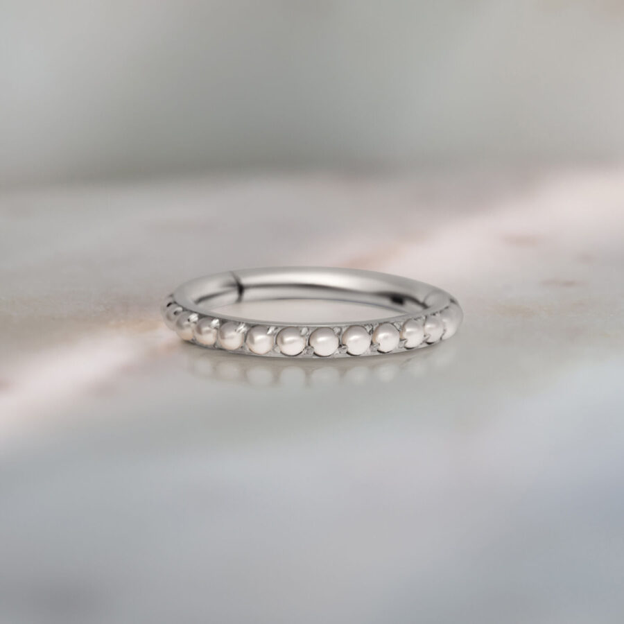 Anillo de piercing plateado con adorno de perlas sobre fondo gris