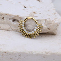 Clicker de septum dorado con diseño en forma de rayos y cristales sobre piedra clara