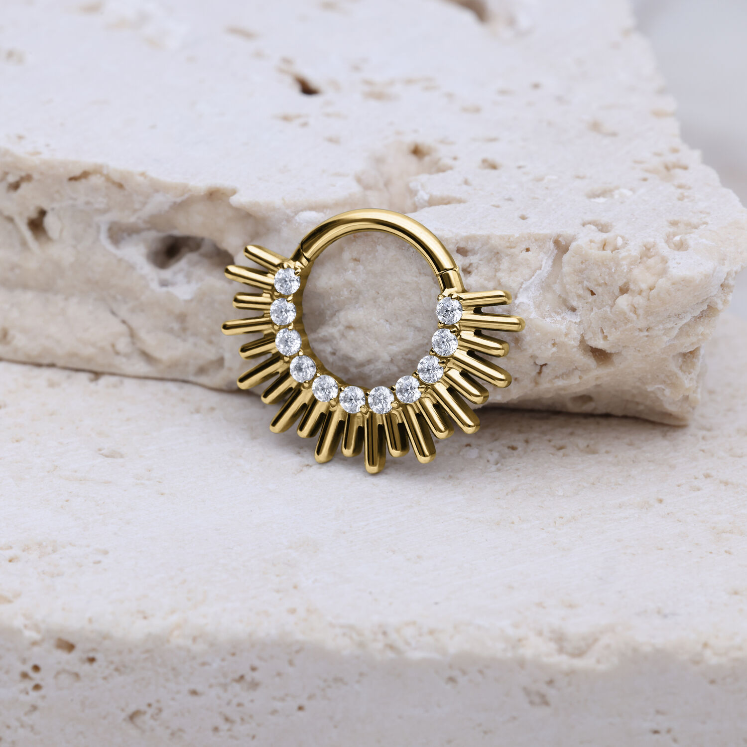 Clicker de septum dorado con diseño en forma de rayos y cristales sobre piedra clara