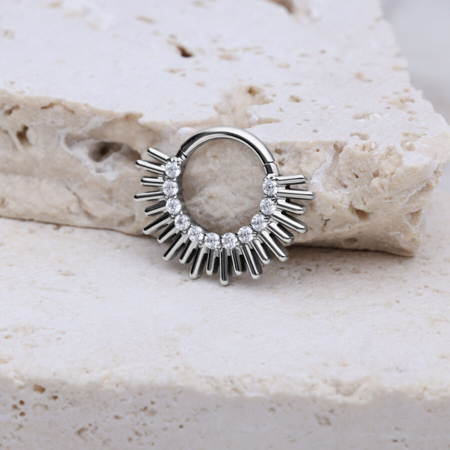 Clicker de septum plateado con diseño de rayos sobre fondo de piedra clara