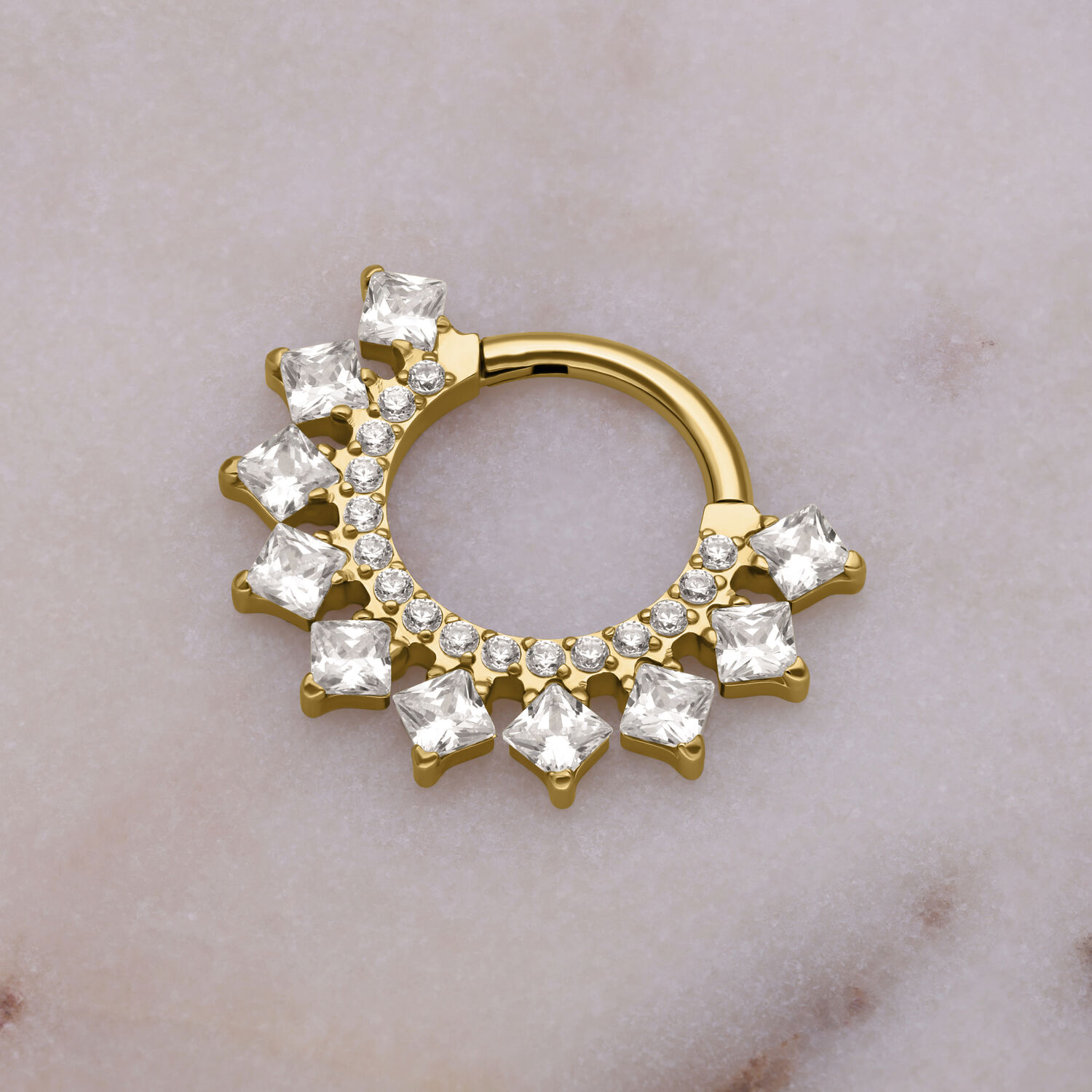 Clicker de septum dorado con adorno de cristal sobre fondo de mármol
