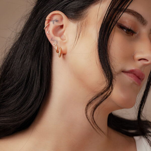 Mujer con colgante de luna en Oro 14K con Moissanita en la oreja sobre fondo neutro