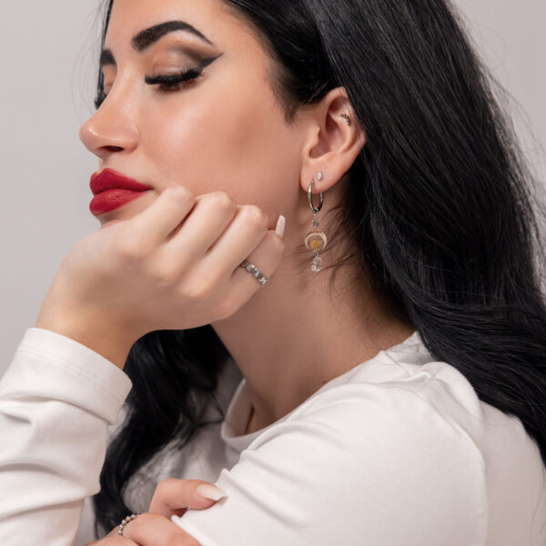Mujer con cabello largo y negro lleva pendientes de acero inoxidable plateados frente a un fondo neutro