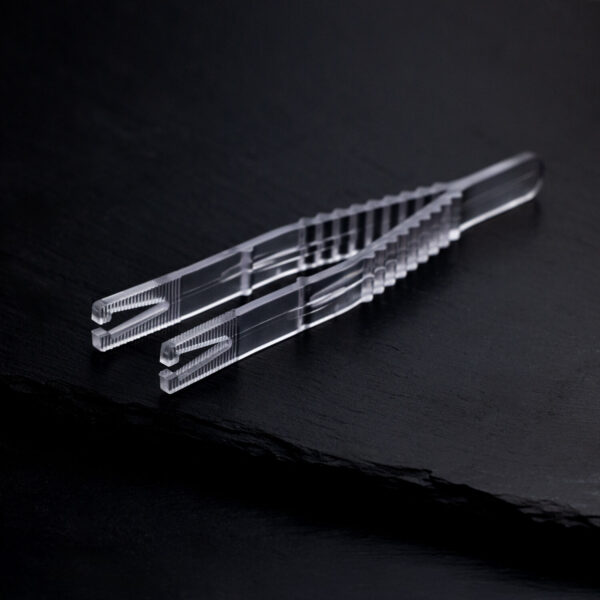 Pinza de piercing triangular clara y estéril sobre fondo negro, empaquetada individualmente