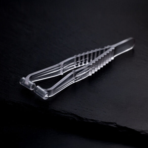 Pinza transparente para piercing de septum de plástico sobre fondo oscuro y liso