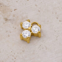 Colgante Trinity de Cristal Dorado con tres cristales claros sobre fondo de piedra beige