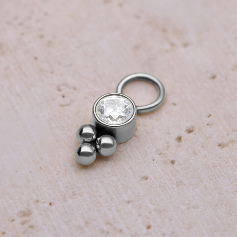 Colgante de piercing plateado con cristal y bolas sobre fondo claro