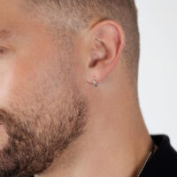 Aros plateados en la oreja de un hombre con barba sobre fondo blanco