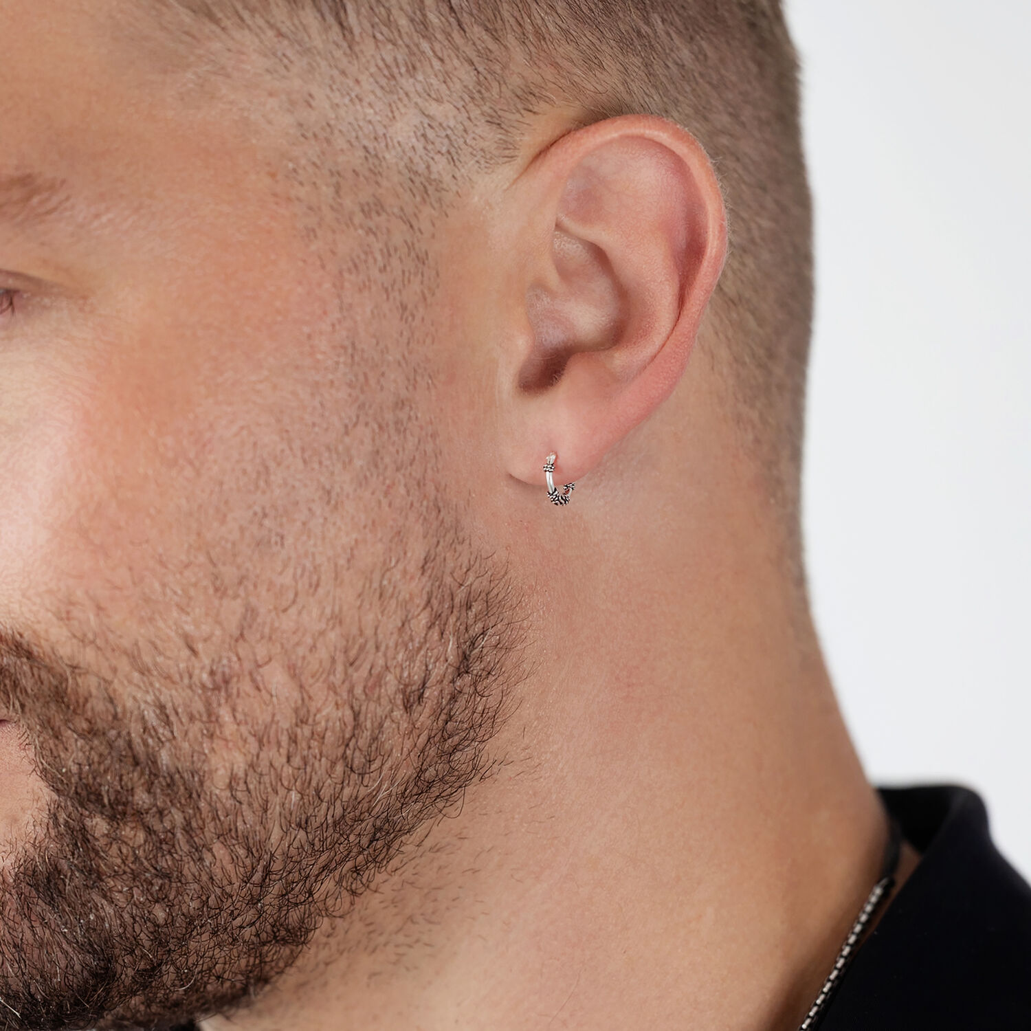 Aros plateados en la oreja de un hombre con barba sobre fondo blanco