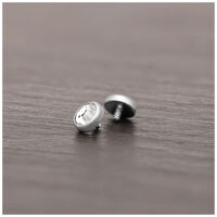 Accesorio de piercing plateado de titanio con cristal claro sobre superficie de madera