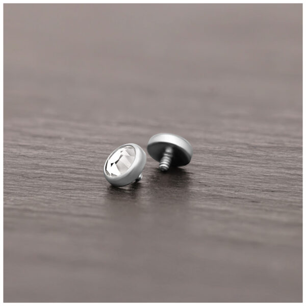 Accesorio de piercing plateado de titanio con cristal claro sobre superficie de madera