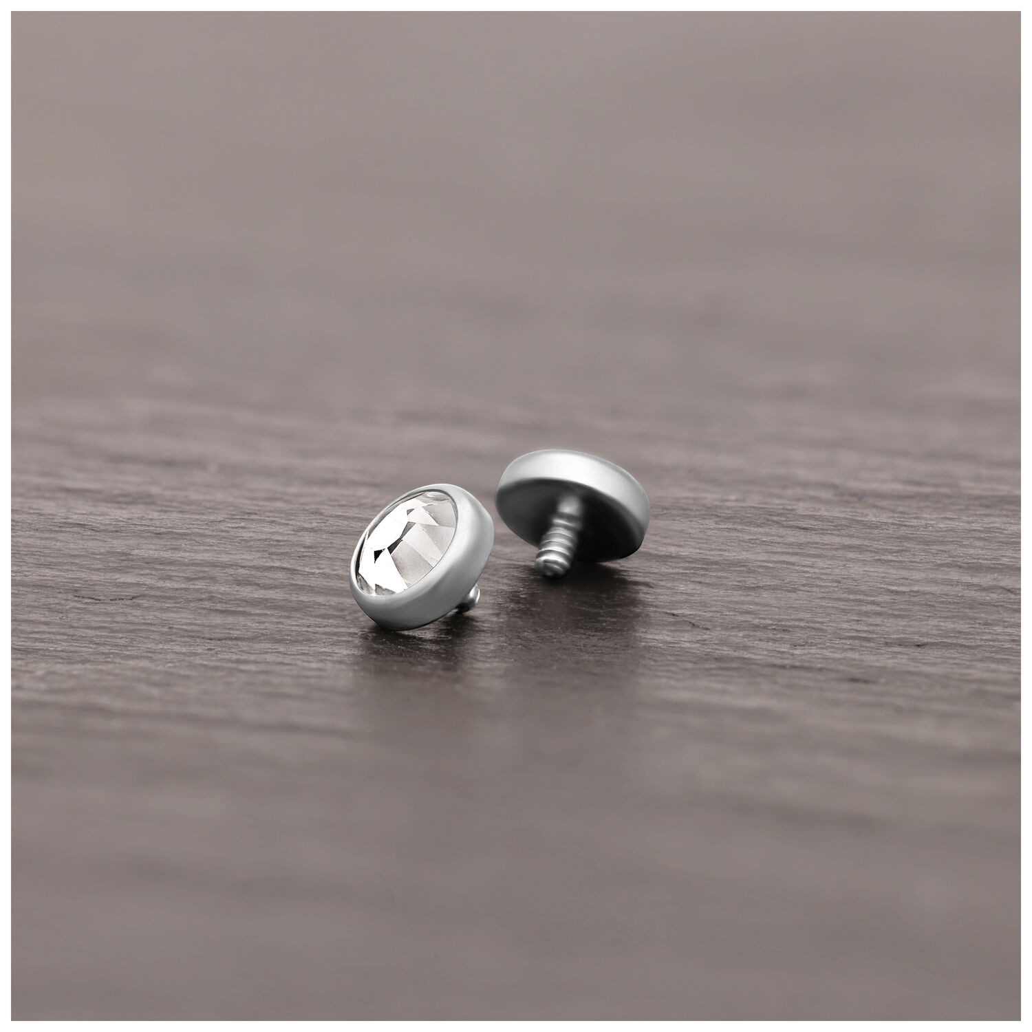 Accesorio de piercing plateado de titanio con cristal claro sobre superficie de madera
