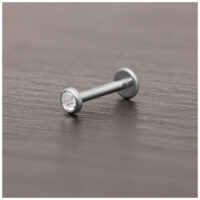 Accesorio de piercing de titanio plateado con cristal claro sobre superficie de madera oscura