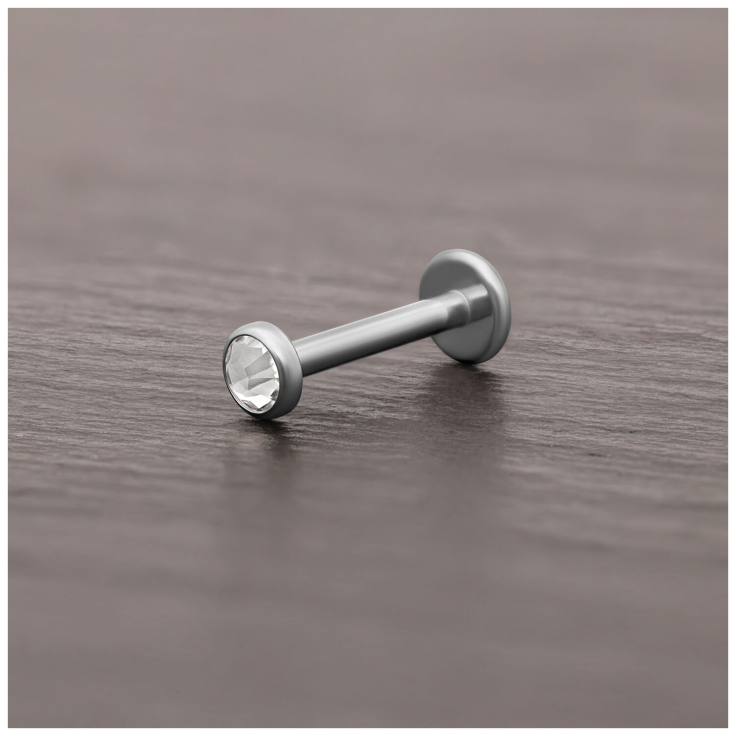 Accesorio de piercing de titanio plateado con cristal claro sobre superficie de madera oscura