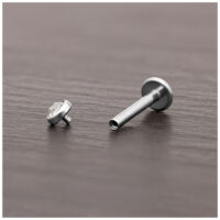 Cabezal de titanio plateado para piercing con cristal claro sobre madera oscura.