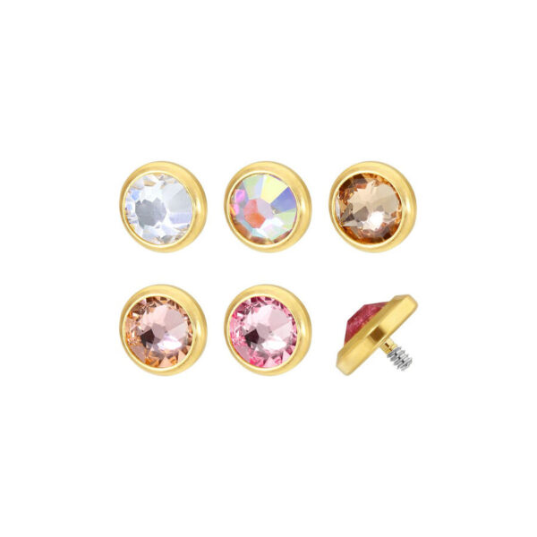 Cinco accesorios de piercing de titanio dorado con cristales claros y de colores sobre fondo blanco