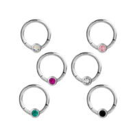 Cinco clickers de septum plateados con cristales de varios colores sobre fondo blanco