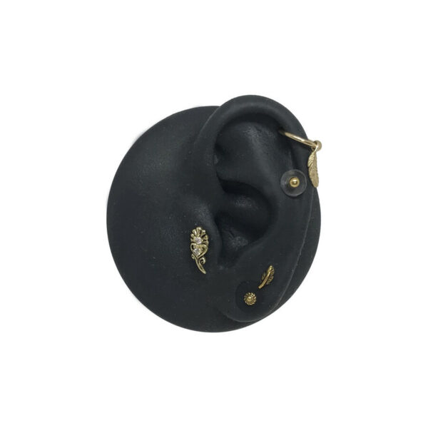 Modelo de oreja de silicona negra con apliques dorados para piercing sobre fondo blanco