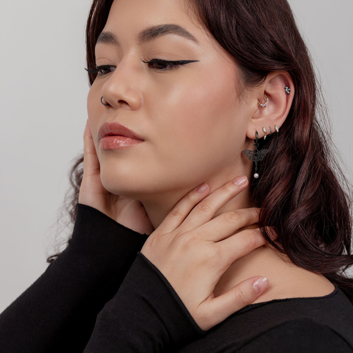Mujer con pendientes de libélula negros y varios piercings en la oreja, perfil lateral